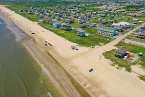 Vista aérea de una zona residencial costera con casas a lo largo de la playa y un edificio azul grande de diseño singular.