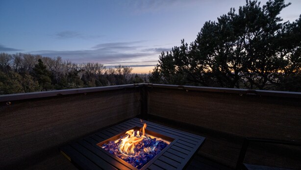 A fire pit in a covered outdoor seating area with a view of trees and a sunset. - Skyview Terrace (Saguache County)