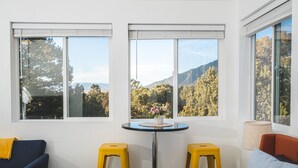 A room with a sofa, two yellow stools, a small table with a vase, and large windows with a mountain view. - Skyview Terrace (Saguache County)
