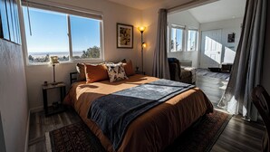 A bedroom with a large bed, a nightstand, a floor lamp, and a view of the outdoors through a window. - Skyview Terrace (Saguache County)