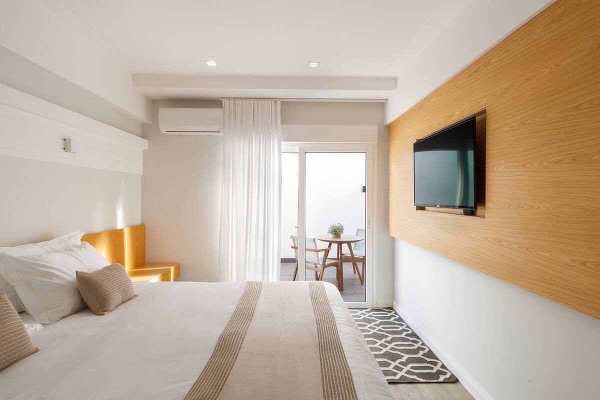 Ein modernes Hotelzimmer mit einem großen Bett, einer Wandpaneele aus Holz, einem Flachbildfernseher und einem Balkon mit Tisch und Stühlen.