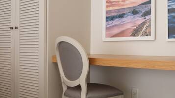 Una habitación con suelo de madera, una silla blanca, una mesa de madera, un armario blanco y dos cuadros en la pared.