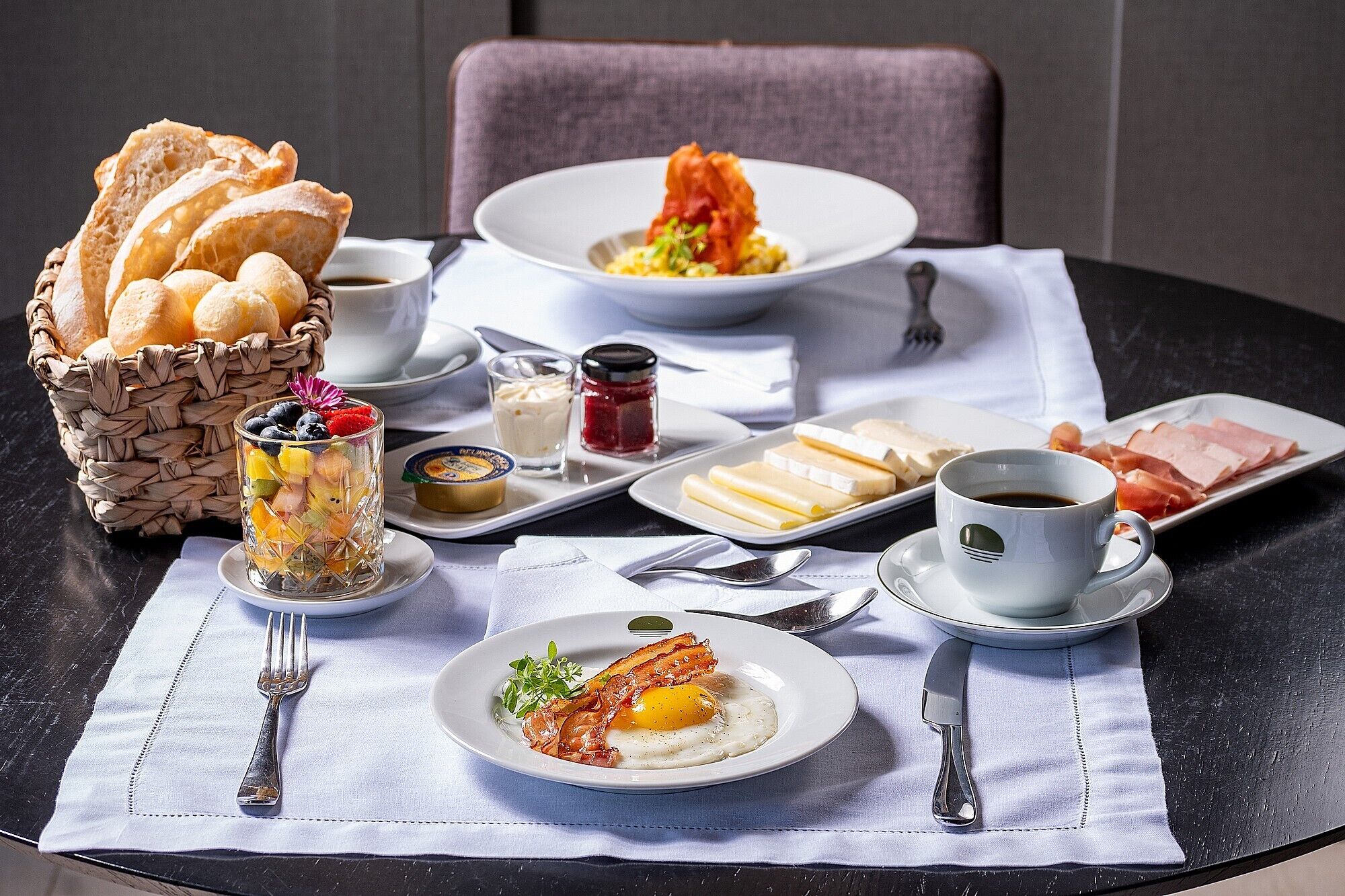 A breakfast setting with bread, eggs, ham, cheese, and coffee on a table.