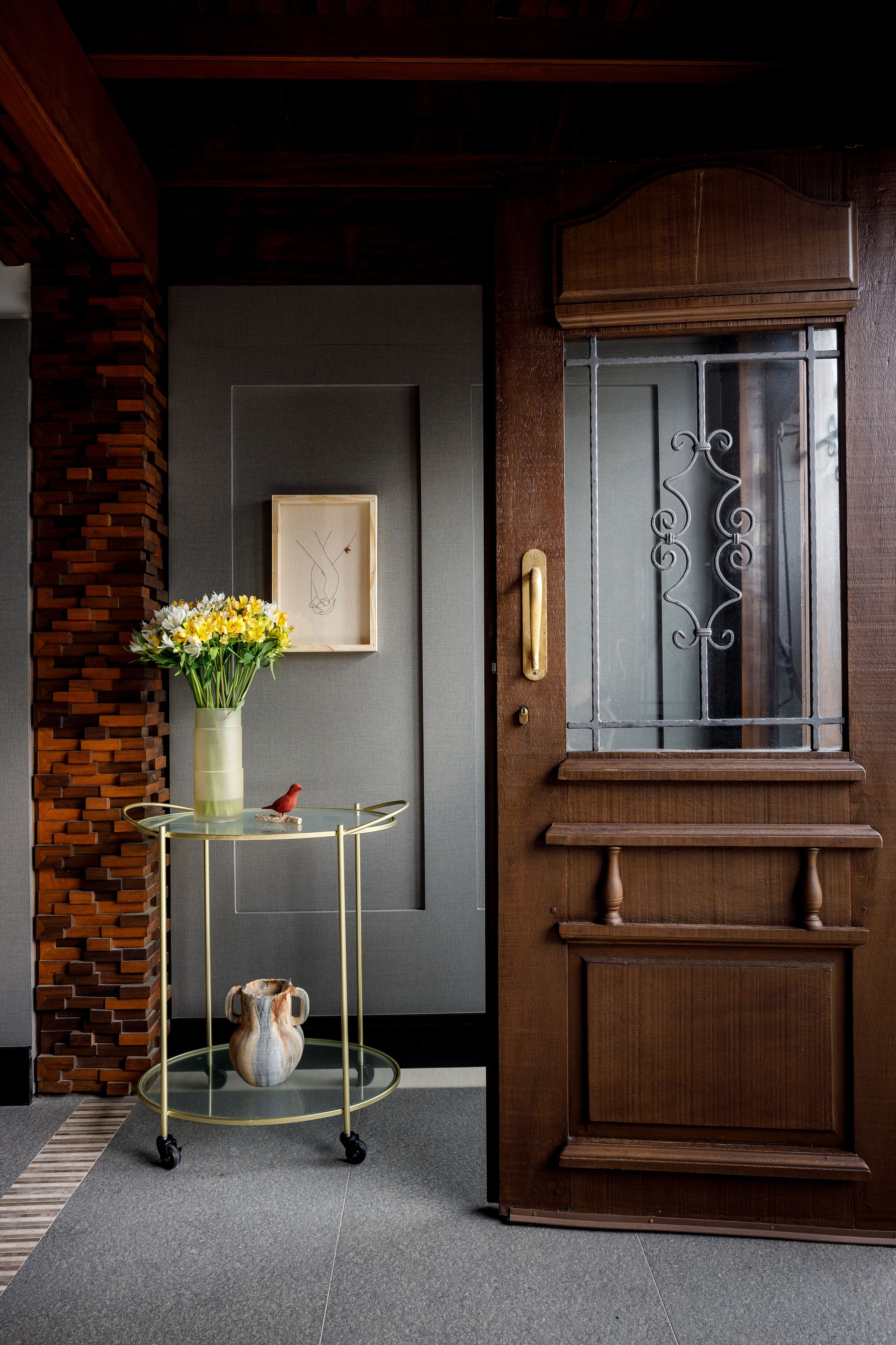 A wooden door with a glass panel and a brass handle, a glass table with a vase of flowers, and a framed picture on the wall.