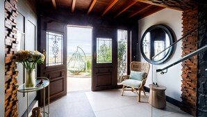 A room with a wooden ceiling, a round window, a wicker chair, and a glass table with a vase of flowers. - Villa d'Ozio Hotel e Cucina (Itajai)