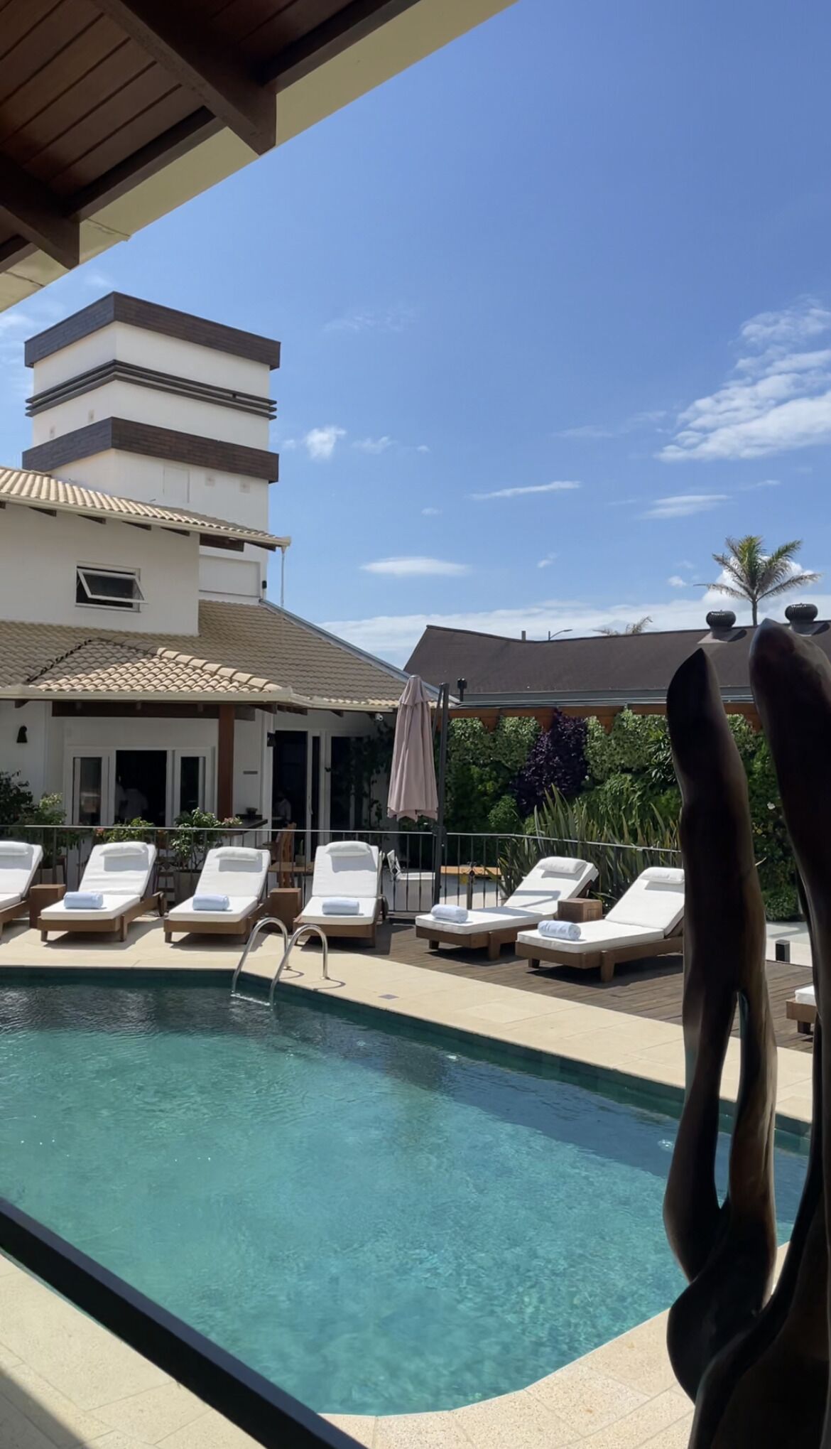 A pool area with lounge chairs and a building with a tiled roof in the background.