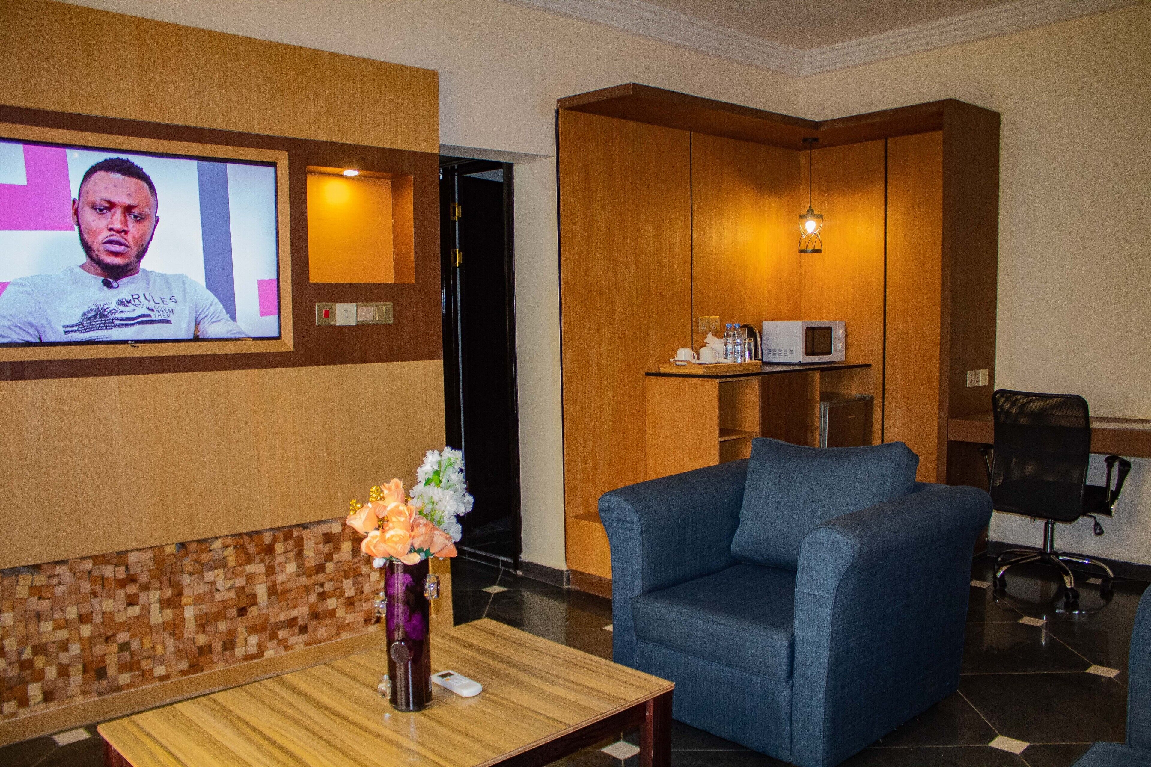 Un moderno vestíbulo de hotel con una televisión, un sofá azul, un armario de madera y una pequeña mesa con un florero.