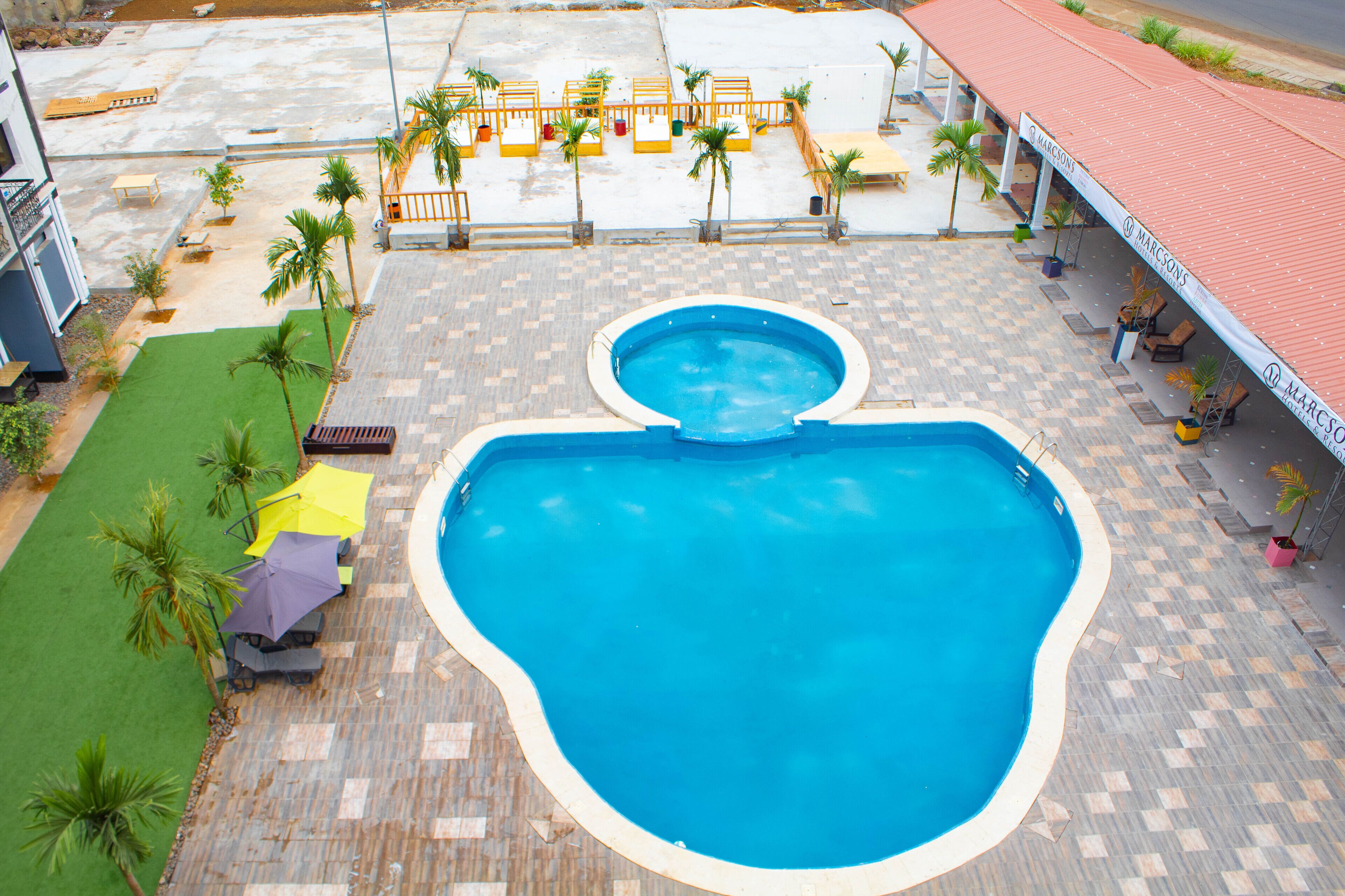 A swimming pool with a tiled deck, surrounded by lounge chairs and umbrellas.
