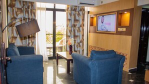 A lobby with two blue armchairs, a wooden reception desk, a TV screen, and a patterned curtain. - Marcsons Hotels and Resorts (Limbe)