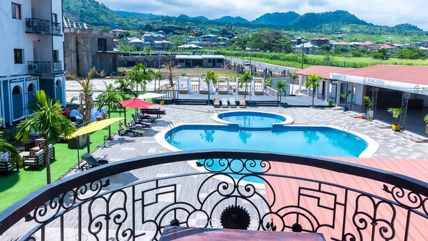 A hotel courtyard with a swimming pool, outdoor seating, and a view of the surrounding landscape. - Marcsons Hotels and Resorts (Limbe)