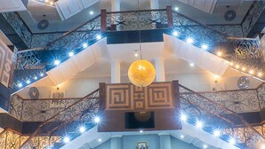 A multi-level interior with ornate railings, a central chandelier, and decorative lighting. - Marcsons Hotels and Resorts (Limbe)
