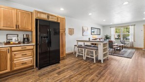 Una cocina con armarios de madera, un refrigerador negro y una zona de comedor con mesa y sillas.