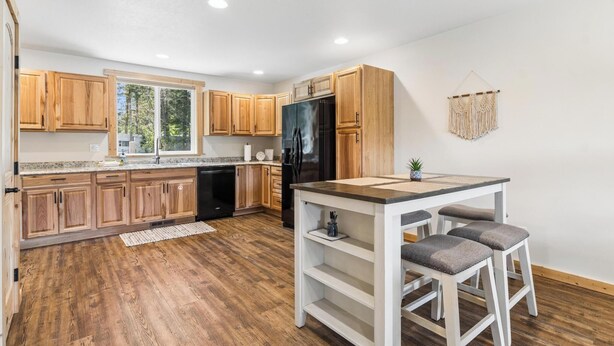 Una cocina moderna con armarios de madera, un refrigerador negro y una pequeña isla con taburetes.