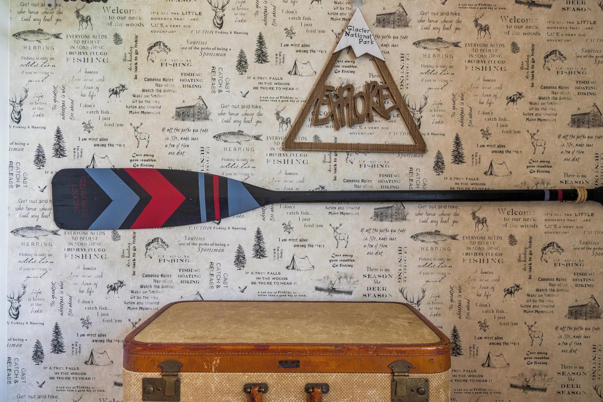 A wooden paddle with a red and blue design, a wooden suitcase, and a wall with text and illustrations related to fishing and nature.