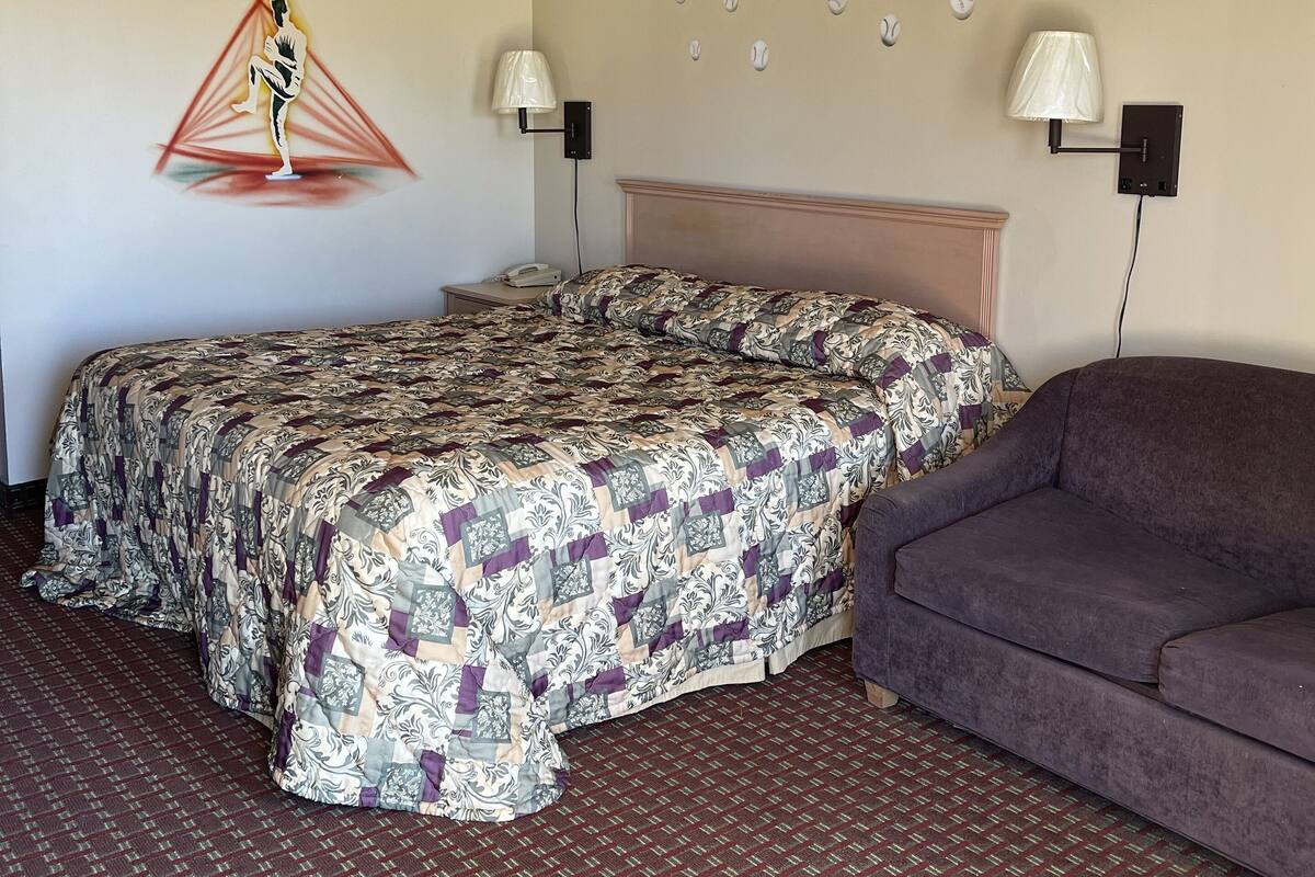A hotel room with a bed, a couch, a wall-mounted lamp, and a ceiling light.