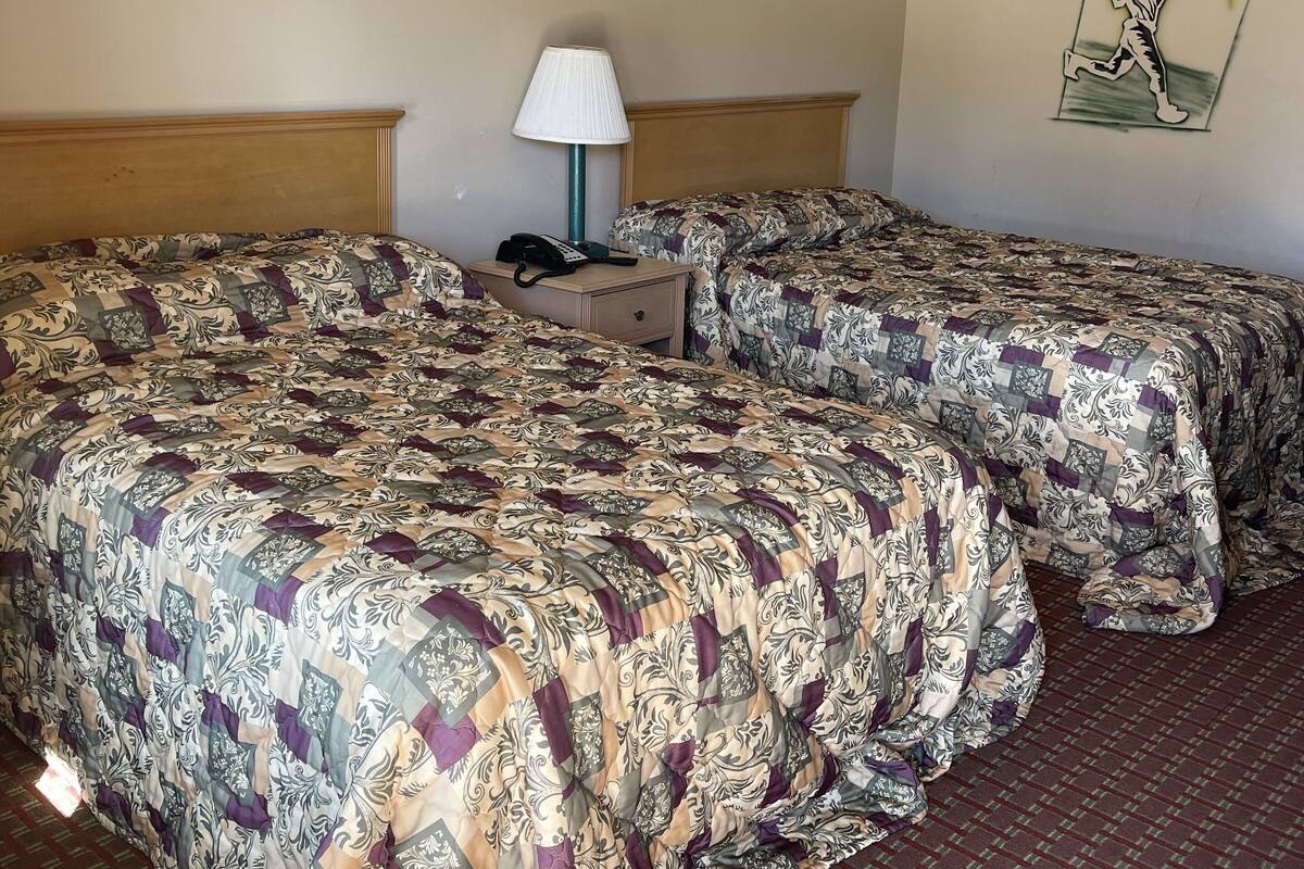A hotel room with two beds, a nightstand, a lamp, and a wall with decorative elements.