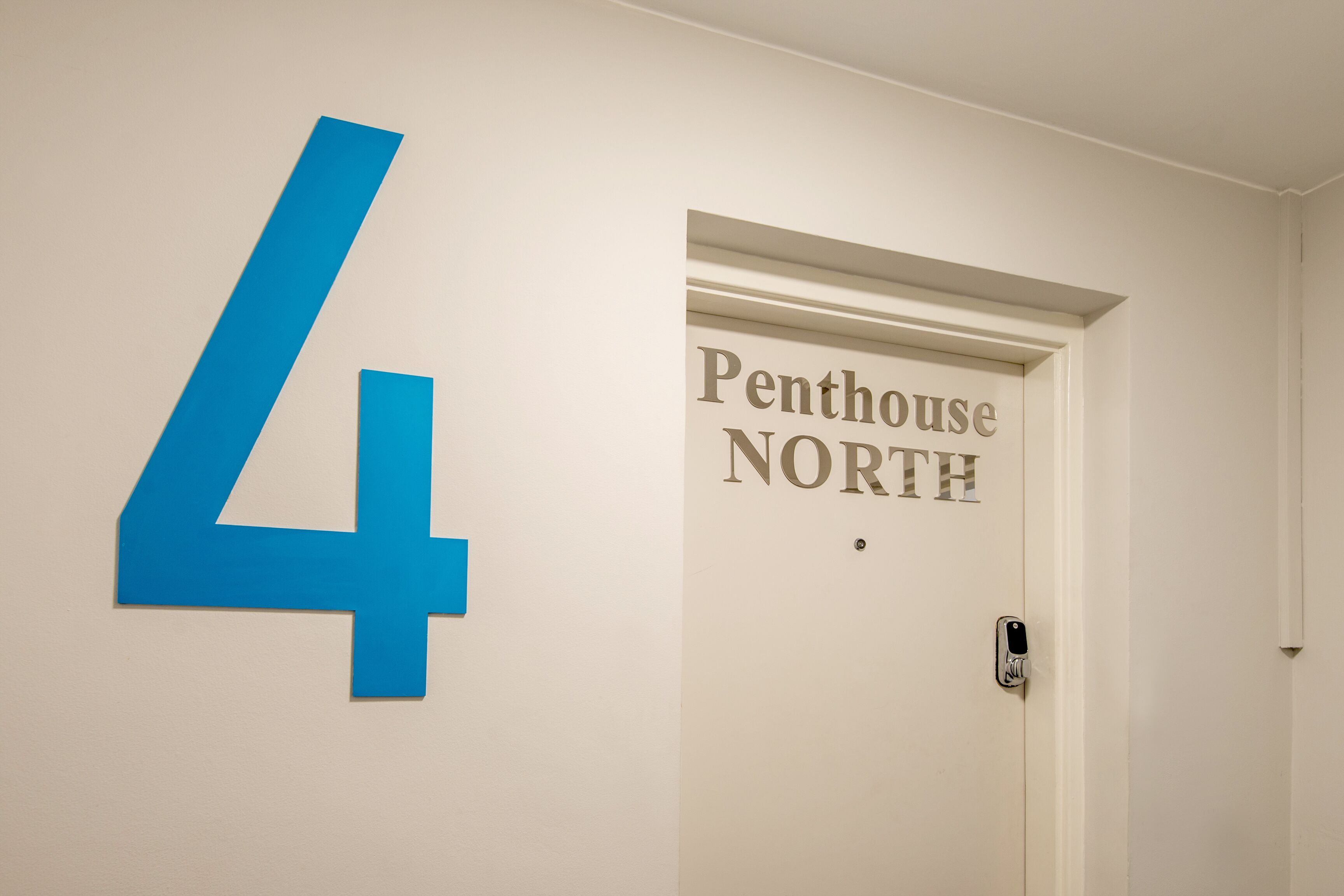 Une porte sur laquelle est apposée une plaque indiquant « Penthouse NORD » et un grand chiffre bleu « 4 » est peint sur le mur.
