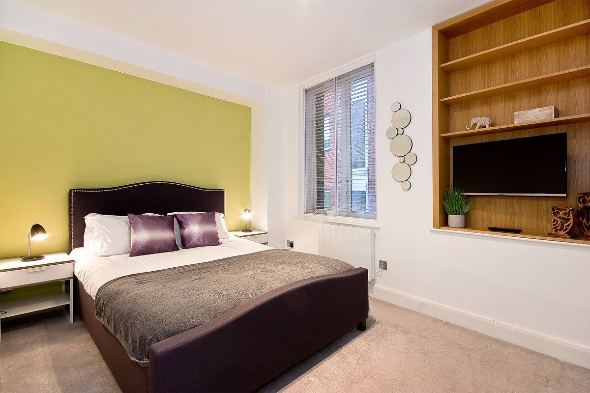 A bedroom with a bed, bedside tables, a TV, and a shelf with decorative items.