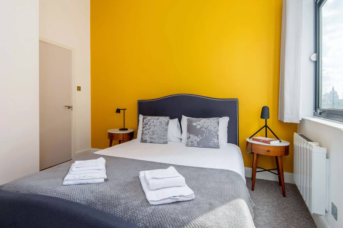 A hotel room with a bed, two bedside tables, a window, and a radiator.