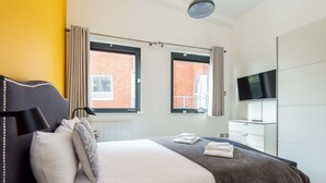 A modern hotel room with a bed, a flat-screen TV, a wardrobe, and two windows with curtains. - Mulberry House London by City Living London (London)