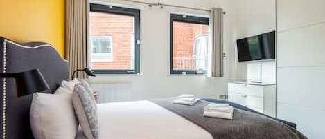 Een moderne hotelkamer met een bed, een flatscreen televisie, een kledingkast en twee ramen met gordijnen.