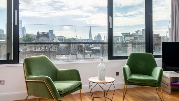 A modern living room with two green armchairs, a small white table, and a large window offering a city view. - Mulberry House London by City Living London (London)