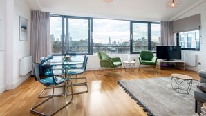 A modern living room with a glass dining table, green chairs, a grey sofa, and a TV. - Mulberry House London by City Living London (London)