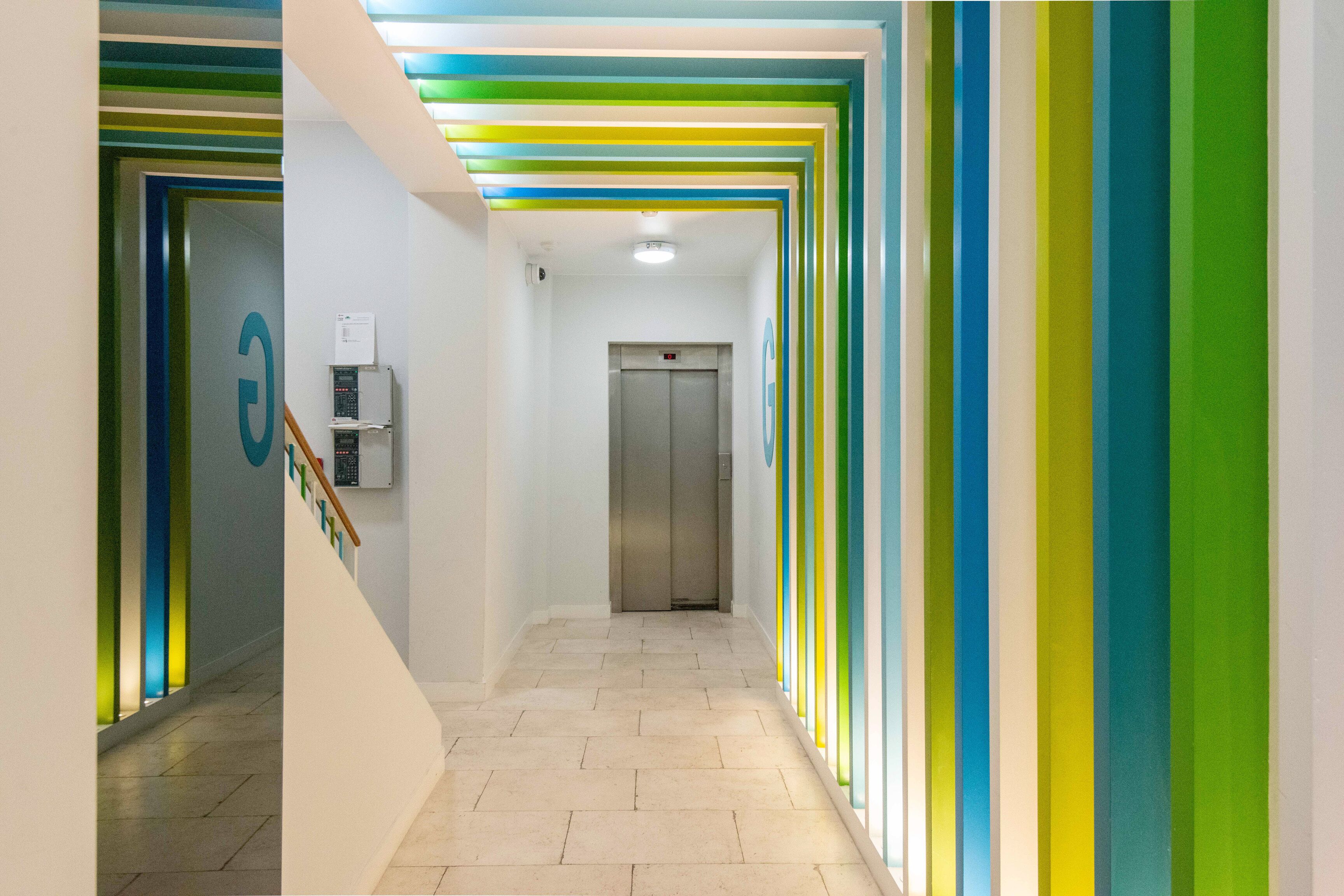 A brightly lit hallway with a staircase on the left and an elevator in the center.