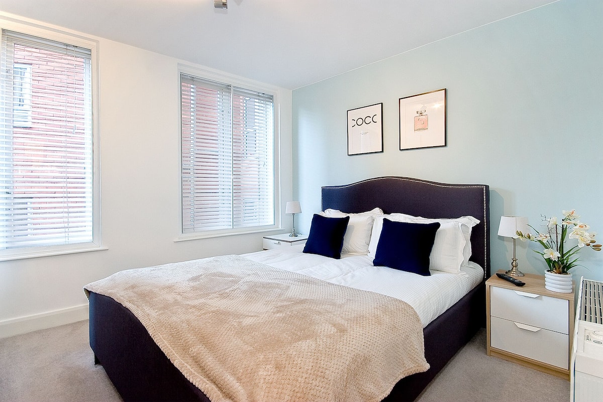 A bedroom with a bed, nightstands, a lamp, and a window with blinds.