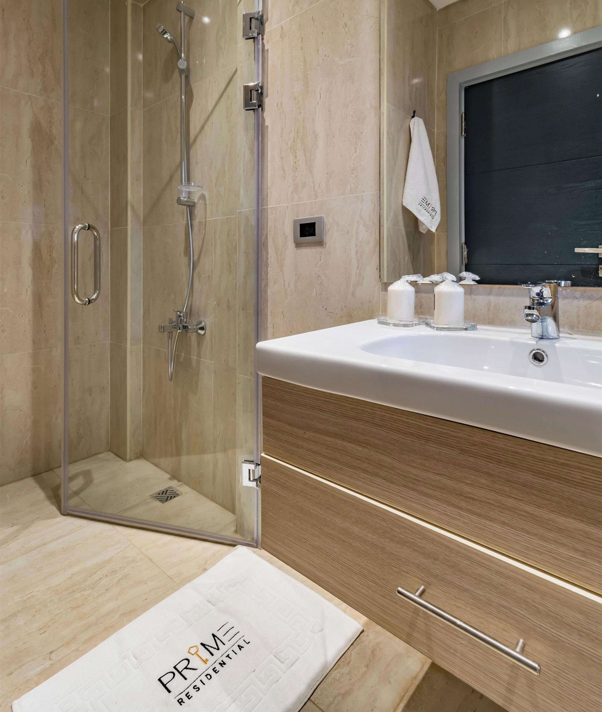 Ein modernes Badezimmer mit einer Duschkabine, einem weißen Waschbecken mit Holzschrank und einem Handtuch an der Wand.
