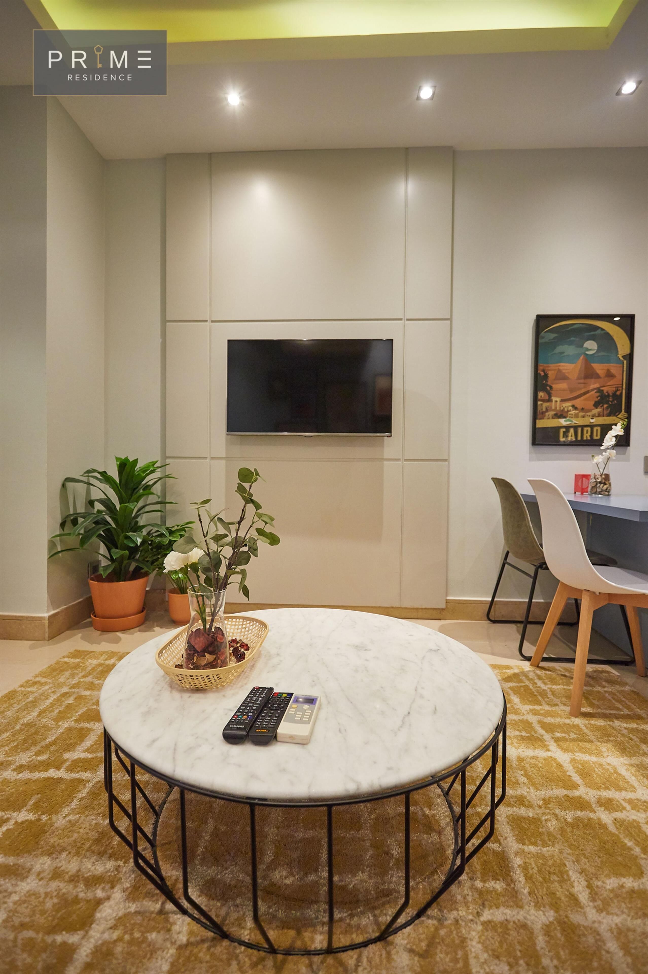 Un saló modern amb una taula de cafè de marbre rodona, un televisor de pantalla plana penjat a la paret, plantes en testos i una zona de menjador amb cadiretes i una taula.