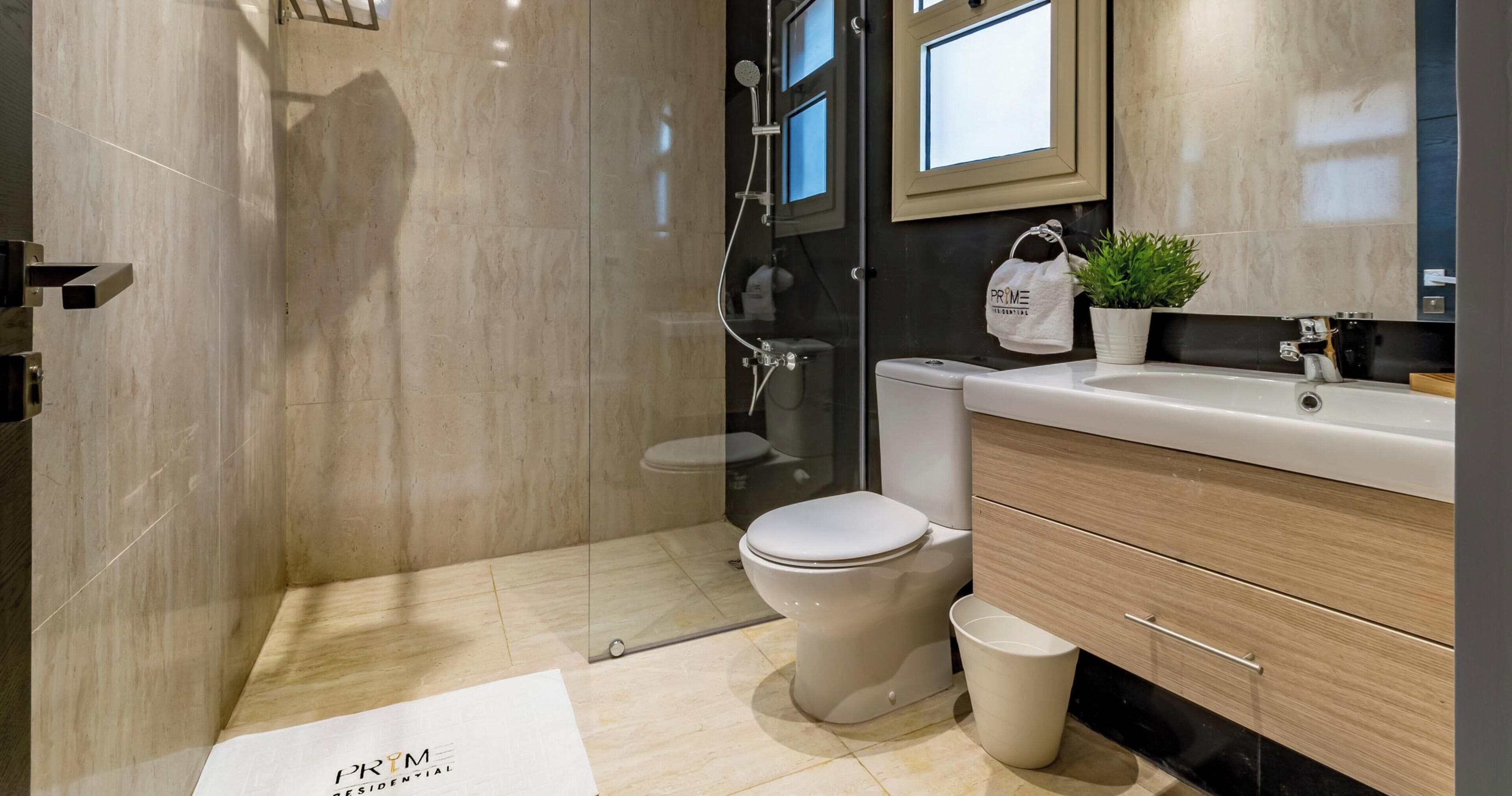 A modern bathroom with a glass-enclosed shower, a toilet, a sink, and a vanity with drawers.