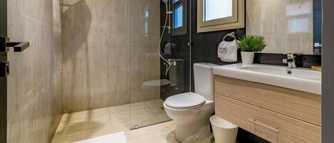 A modern bathroom with a glass-enclosed shower, a toilet, a sink, and a vanity with drawers.