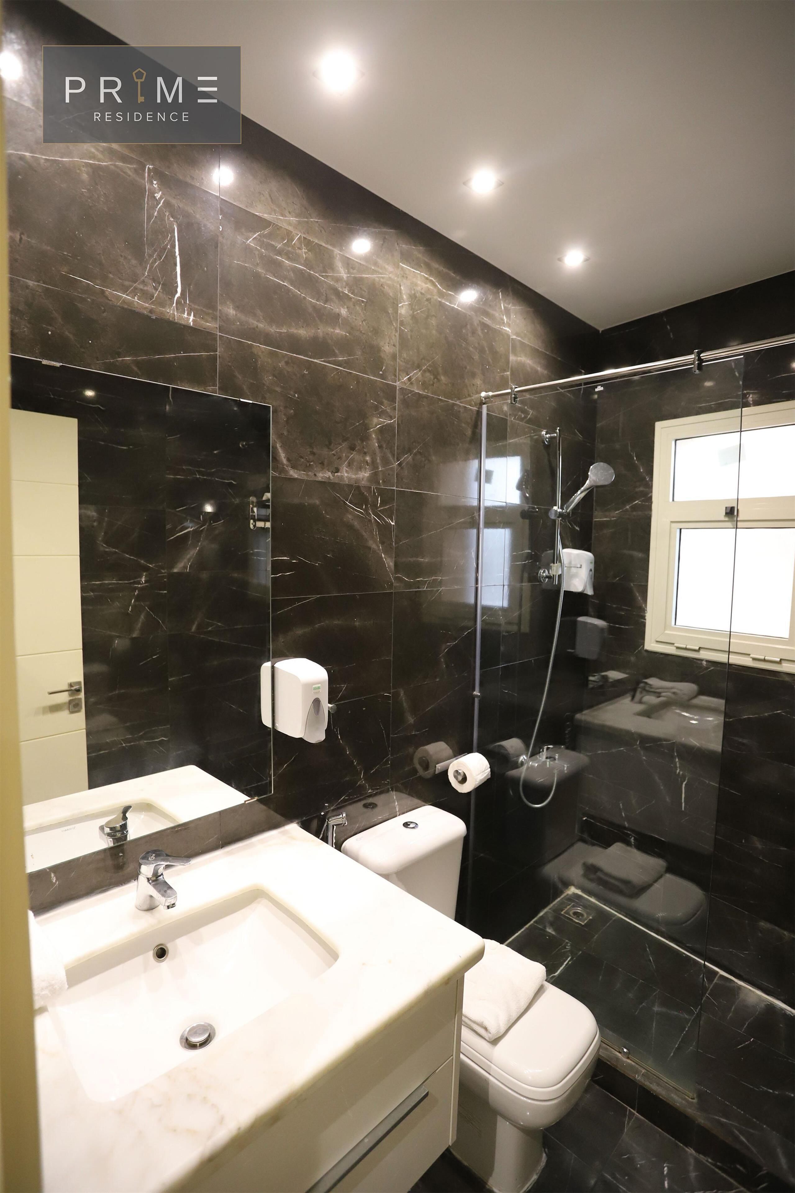A modern bathroom with a marble backsplash, a glass-enclosed shower, a white sink, and a toilet.