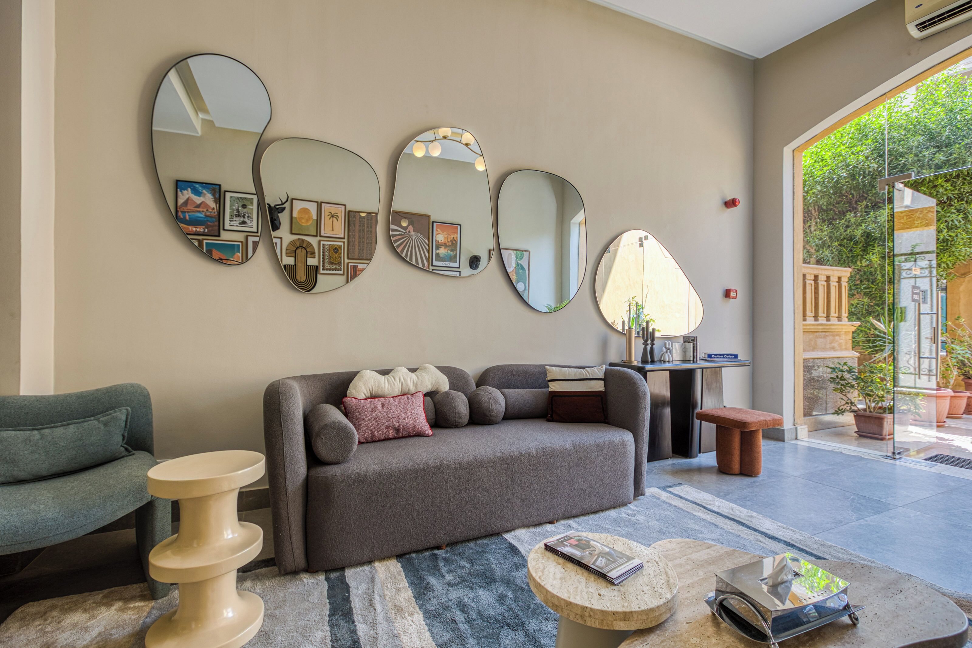 Sala de estar con un sofá gris, una mesa redonda de centro y un sillón azul. Hay tres espejos montados en la pared y una mesita auxiliar pequeña.