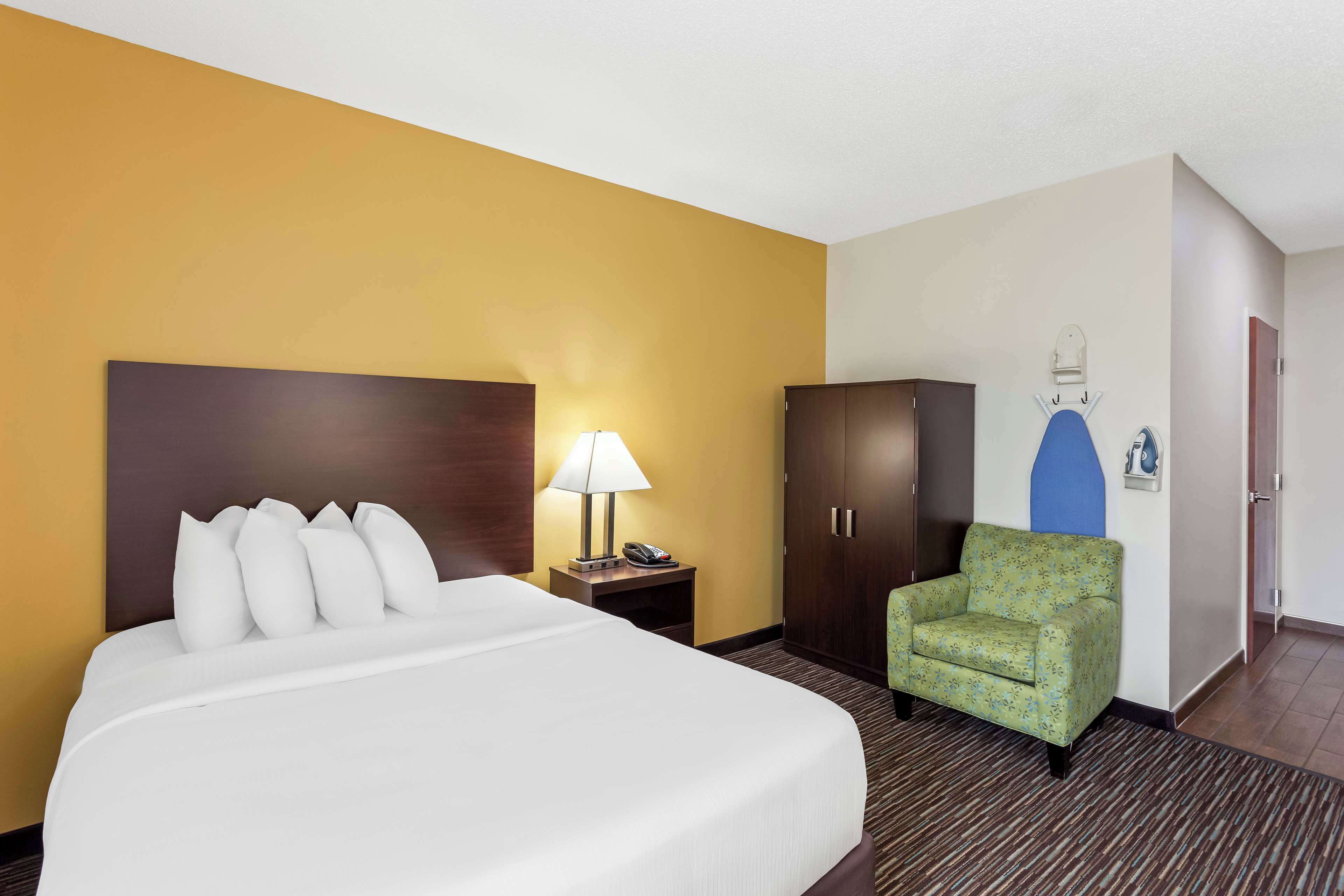 A hotel room with a large bed, a nightstand with a lamp, a green armchair, and a wardrobe.