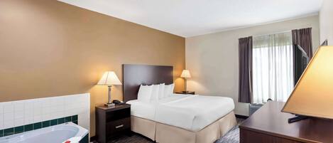 A hotel room with a large bed, a bedside table with lamps, a TV, a window with curtains, and a bathtub.