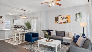 Un salon moderne avec un coin repas, un ventilateur de plafond et une cuisine en arrière-plan.
