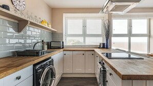 A modern kitchen with a built-in washing machine, a microwave, and a large window with blinds.