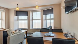 A modern room with a wooden table, black chairs, a sofa, and a TV mounted on the wall.