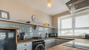 A modern kitchen with a built-in dishwasher, a microwave, and a sink. There is a clock on the wall and a window with blinds.