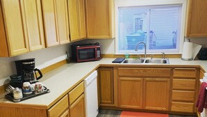 Una cocina compacta con armarios de madera, un microondas, una cafetera y un lavamanos.
