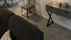 Una sala de estar con un sofá marrón oscuro, una silla de madera, un escritorio con una lámpara y un reloj de pared.