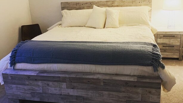 Una cama con cabecera de madera, ropa de cama blanca y una manta azul.