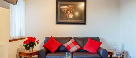 A living room with a sofa, a coffee table, a framed picture on the wall, and a window with blinds.