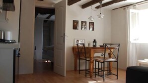 Un coin repas avec une table et des chaises en bois, une cuisine équipée d’une cuisinière, et une porte donnant sur une autre pièce.