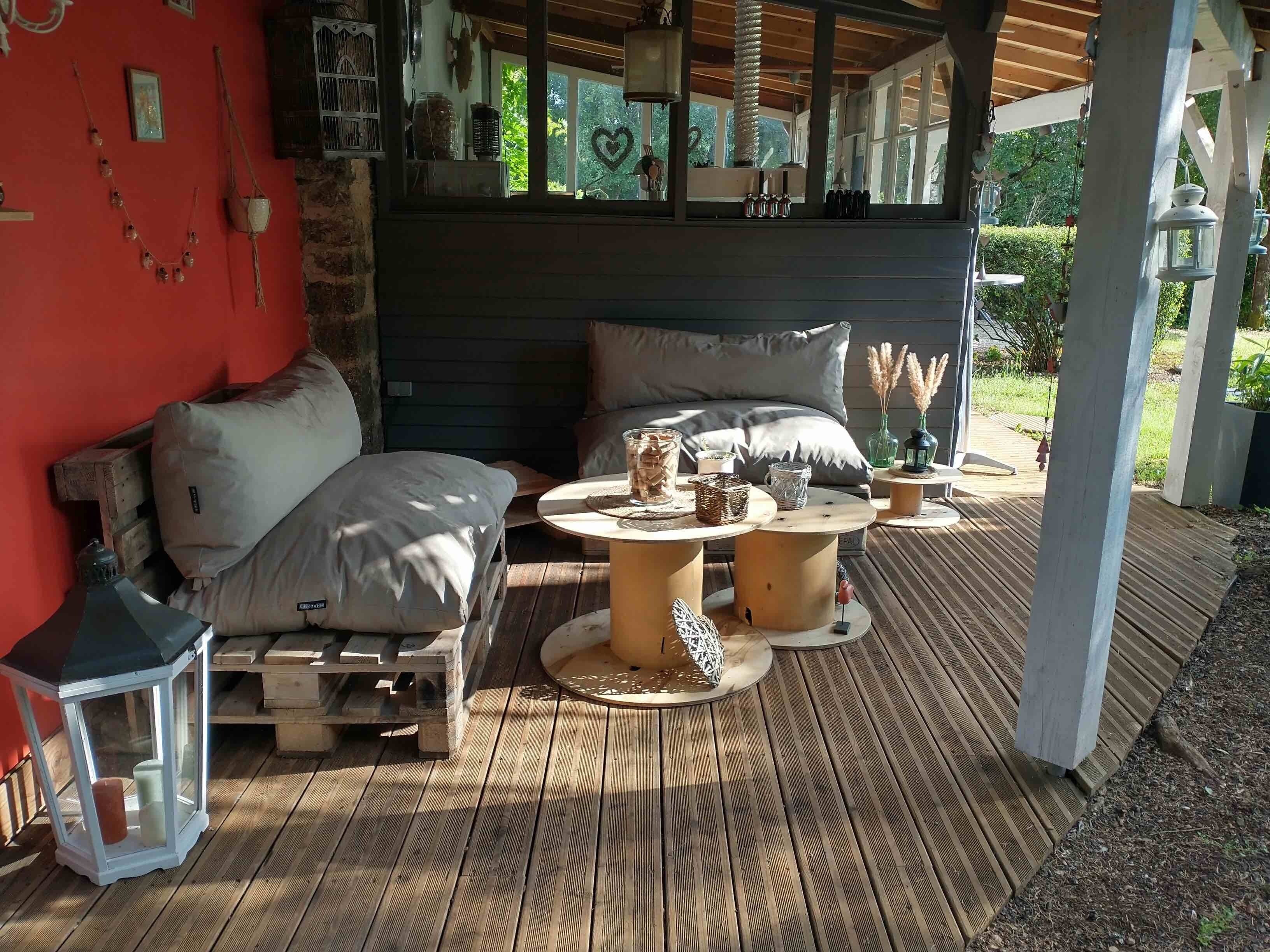 A covered outdoor seating area with a wooden deck, a sofa, and a table with decorative items.