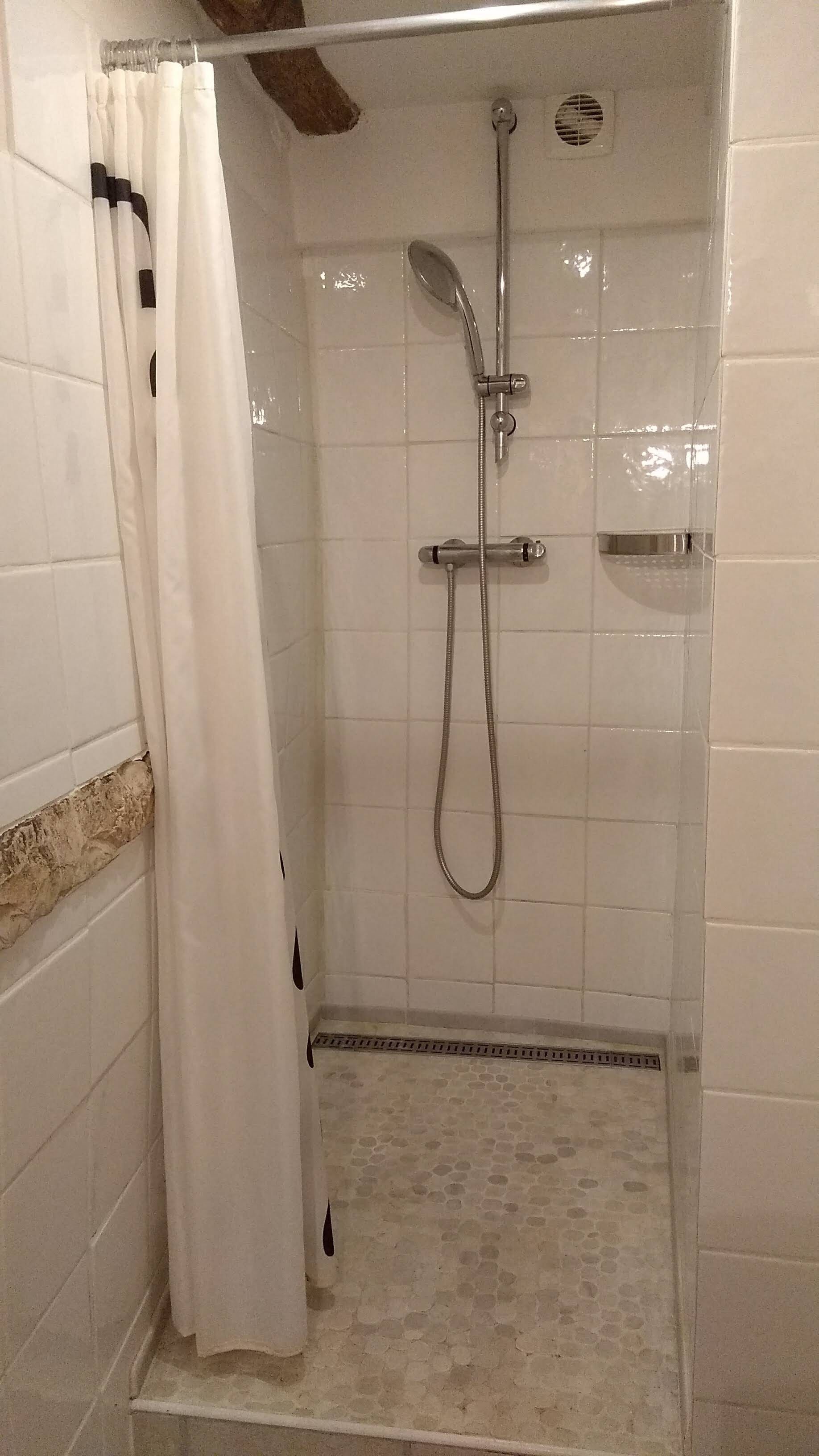 Ducha con cabezal de ducha manual y otro fijo, paredes con azulejos y cortina blanca.