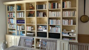 Une pièce comprenant une grande bibliothèque remplie de livres, une table à manger avec des chaises et un buffet blanc.