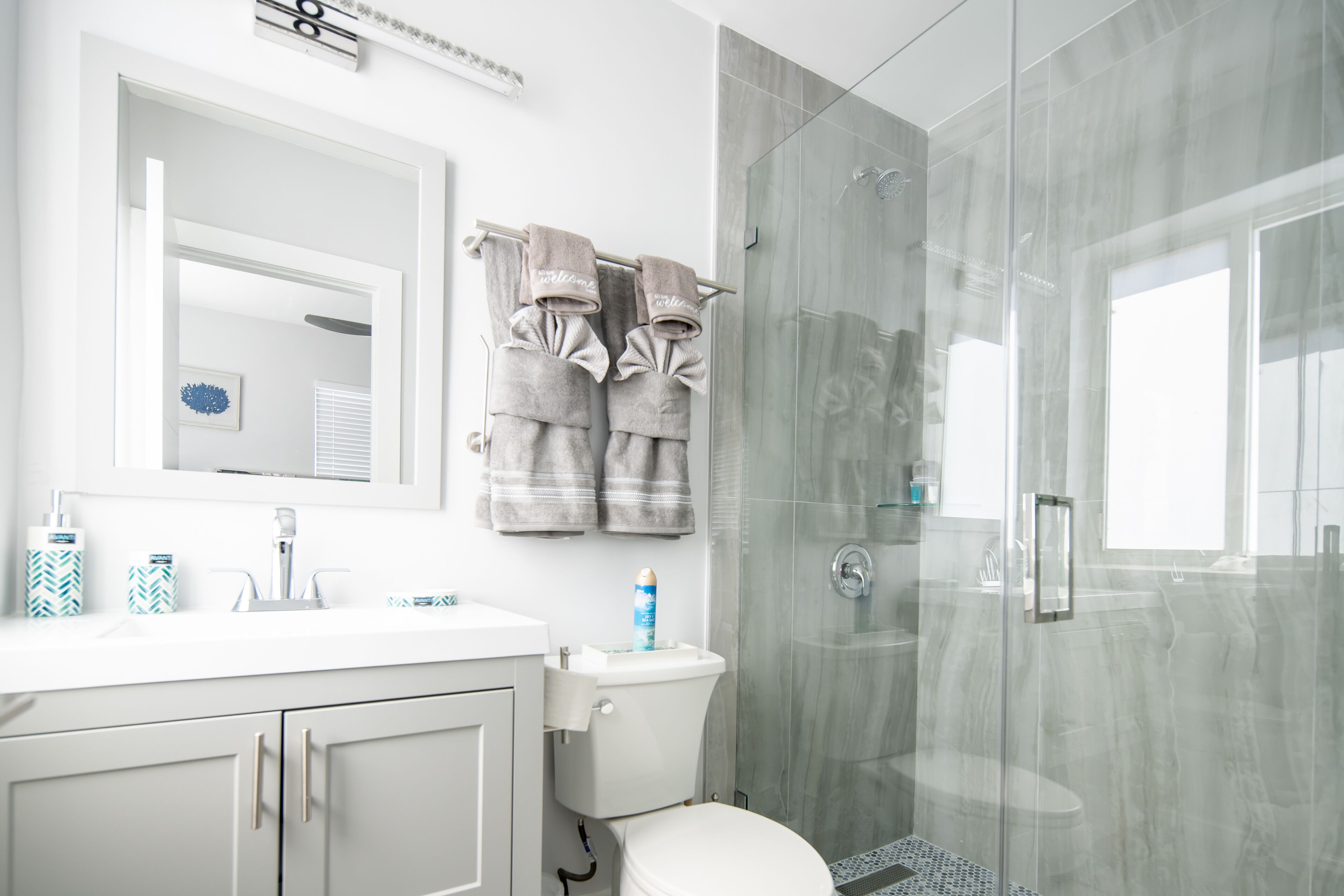 Un baño moderno con cabina de ducha de vidrio, un lavamanos blanco con espejo y dos toallas colgadas en un perchero.